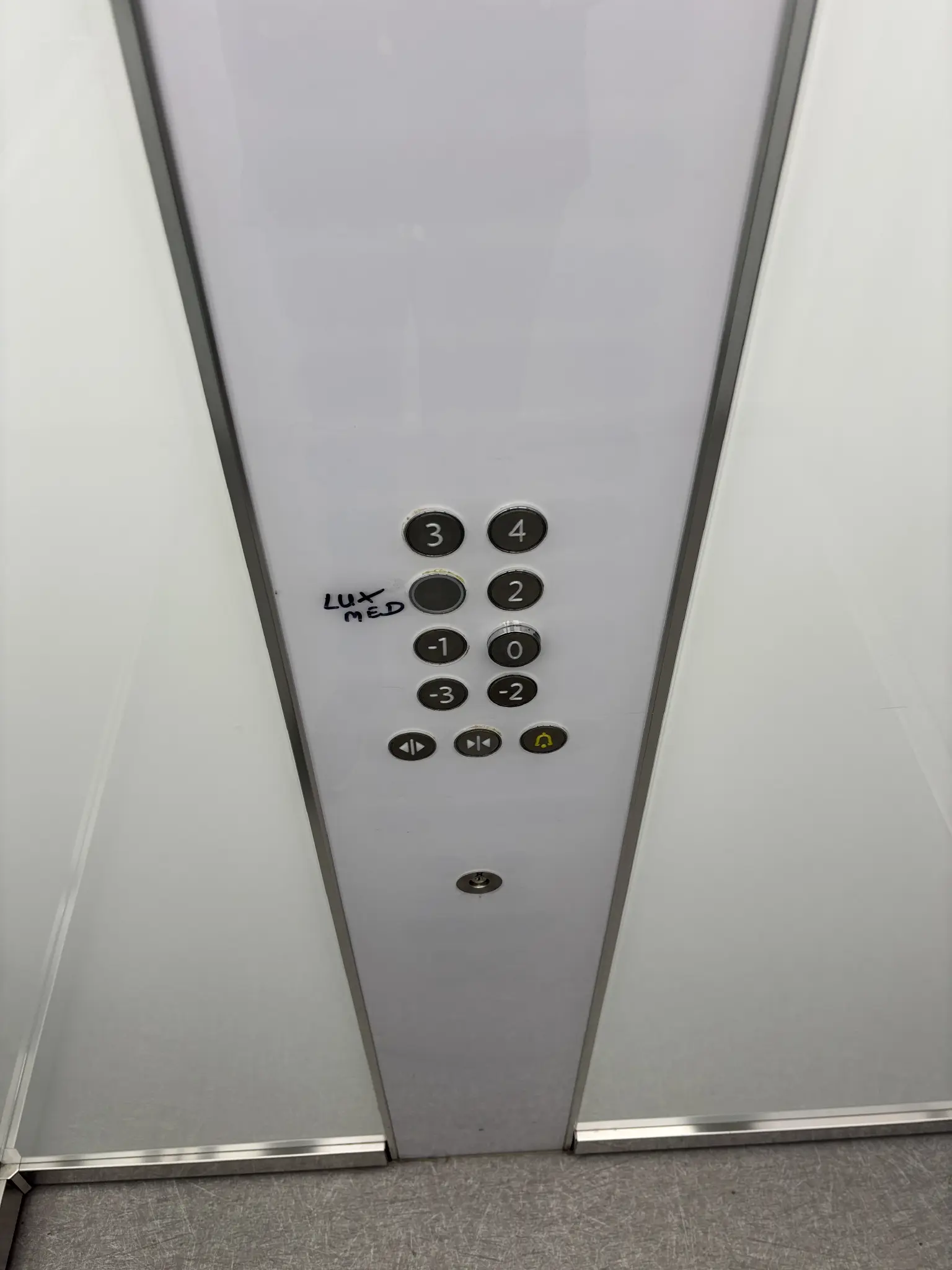 an elevator with an array of buttons. one of the buttons isn’t numbered and has “lux med” hastily scribbled next to it with what looks like permanent marker