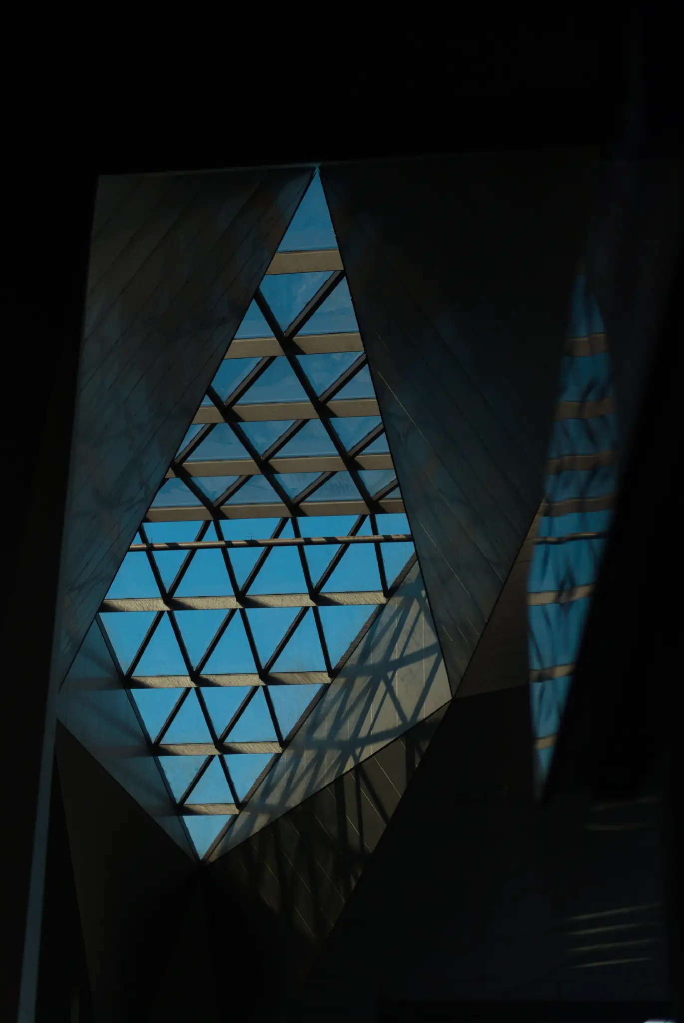 a ceiling with a window in it. there's loads of very odd angles, and every surface is a triangle. the window is subdivided into many smaller triangles, with relatively deep support beams, which cast interesting shadows on the surfaces below. an out of focus sign in the foreground is reflecting the window.